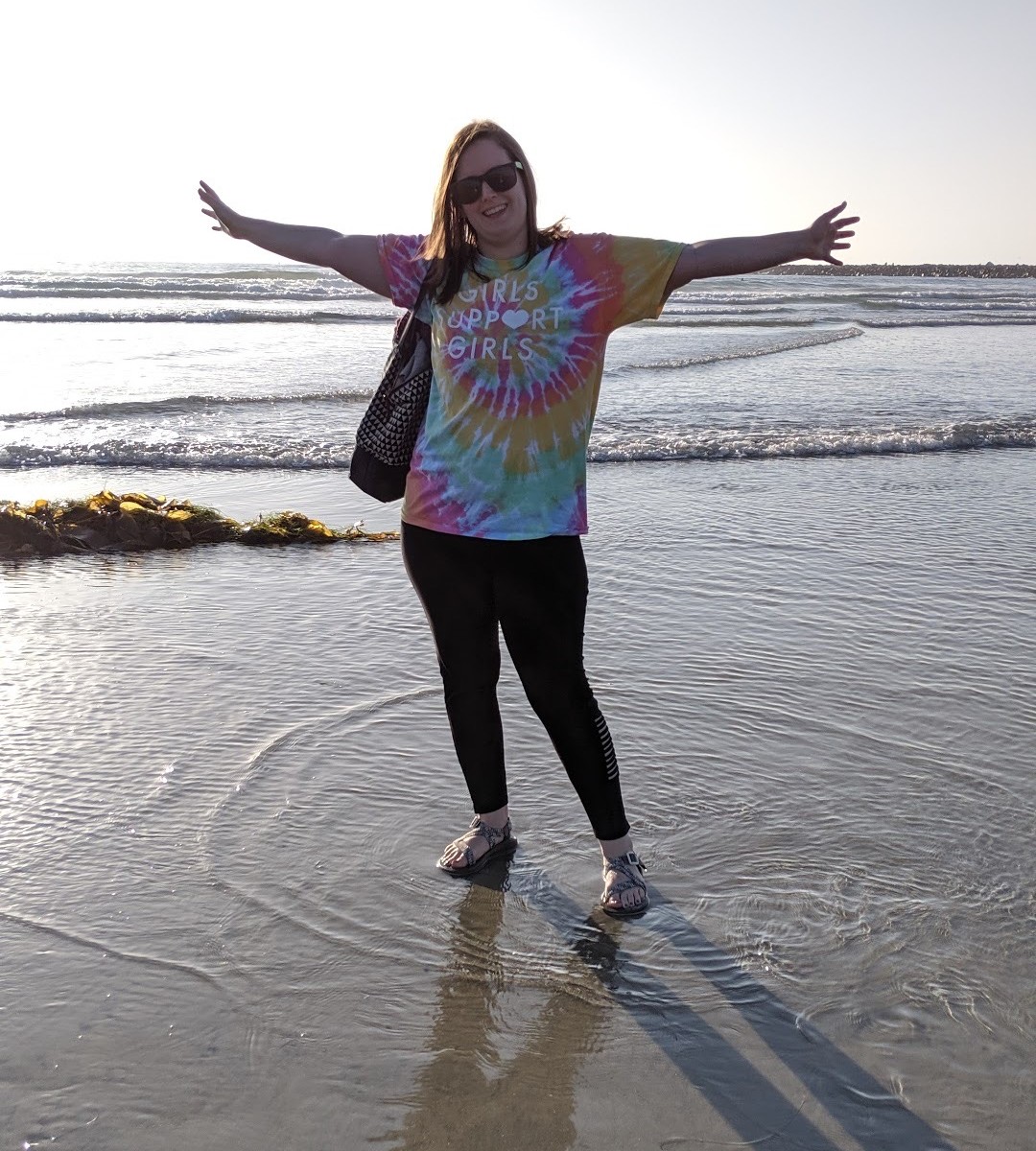 Lea at the beach with arms outstretched wearing Girls Support Girls shirt